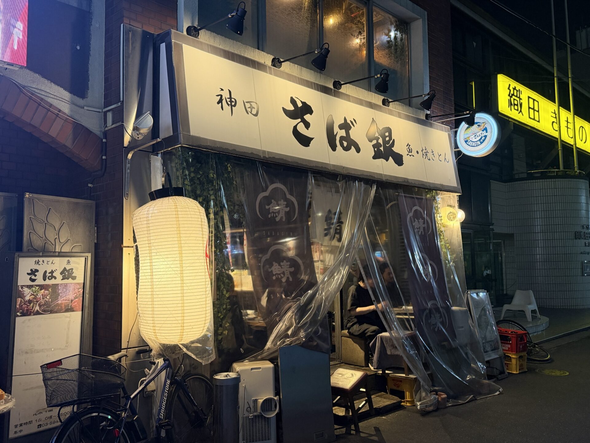 The night-time facade of Saba-Gin Nakano, with its dark signboard and a white paper lantern over the entrance