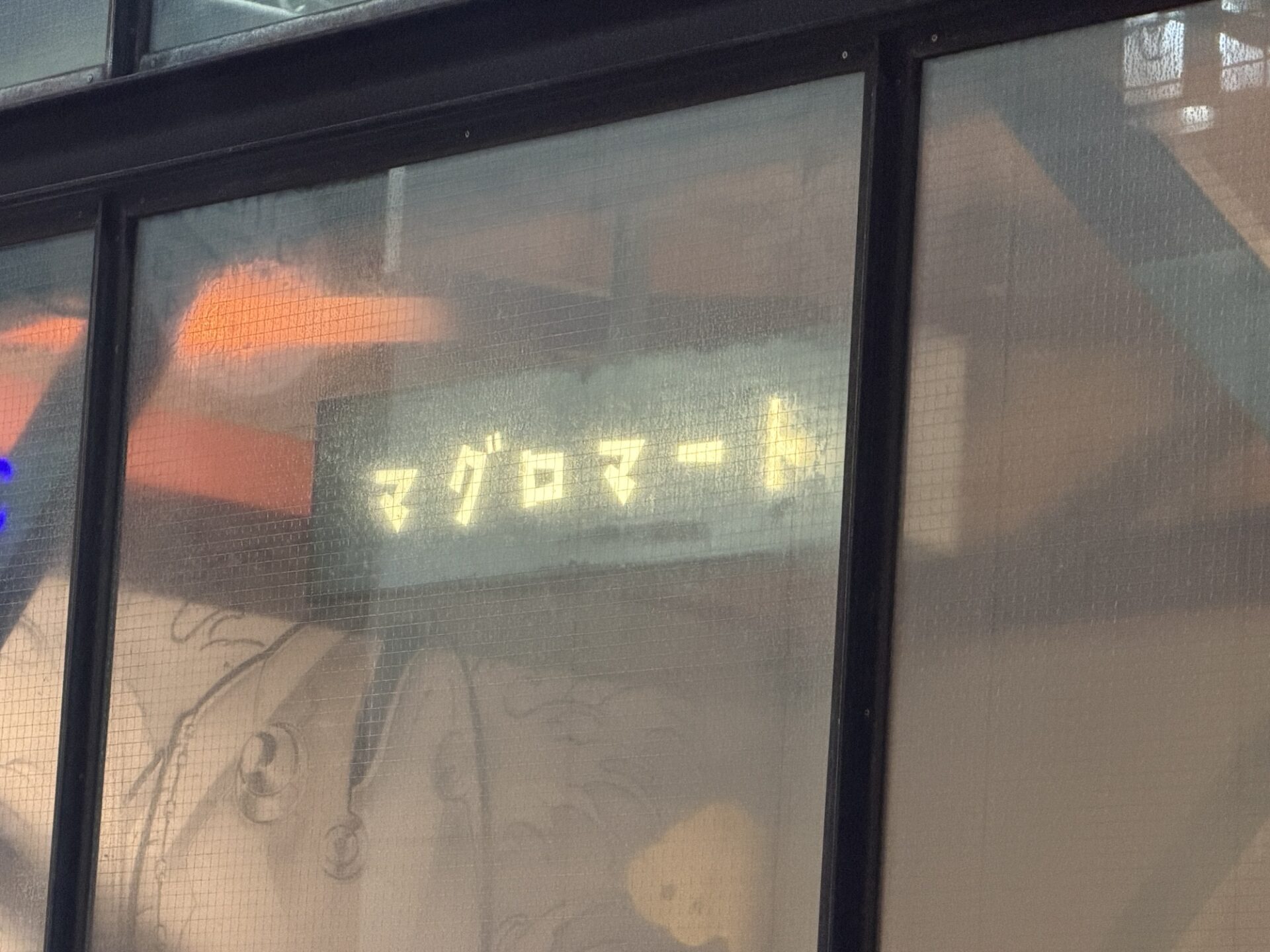The Maguro Mart neon sign seen through the shop's frosted window